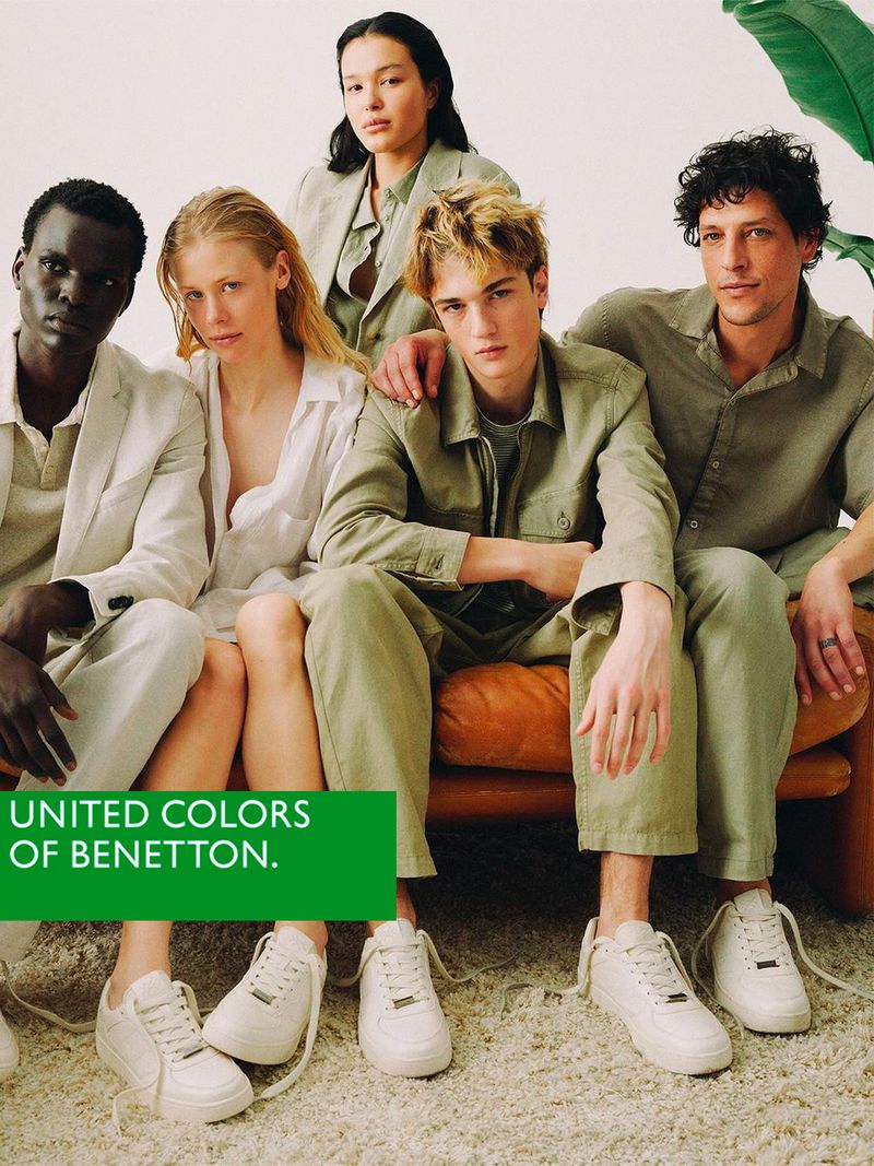 Group of diverse models showcasing neutral-toned casual clothing and white sneakers, seated on a brown sofa, against a clean white background.