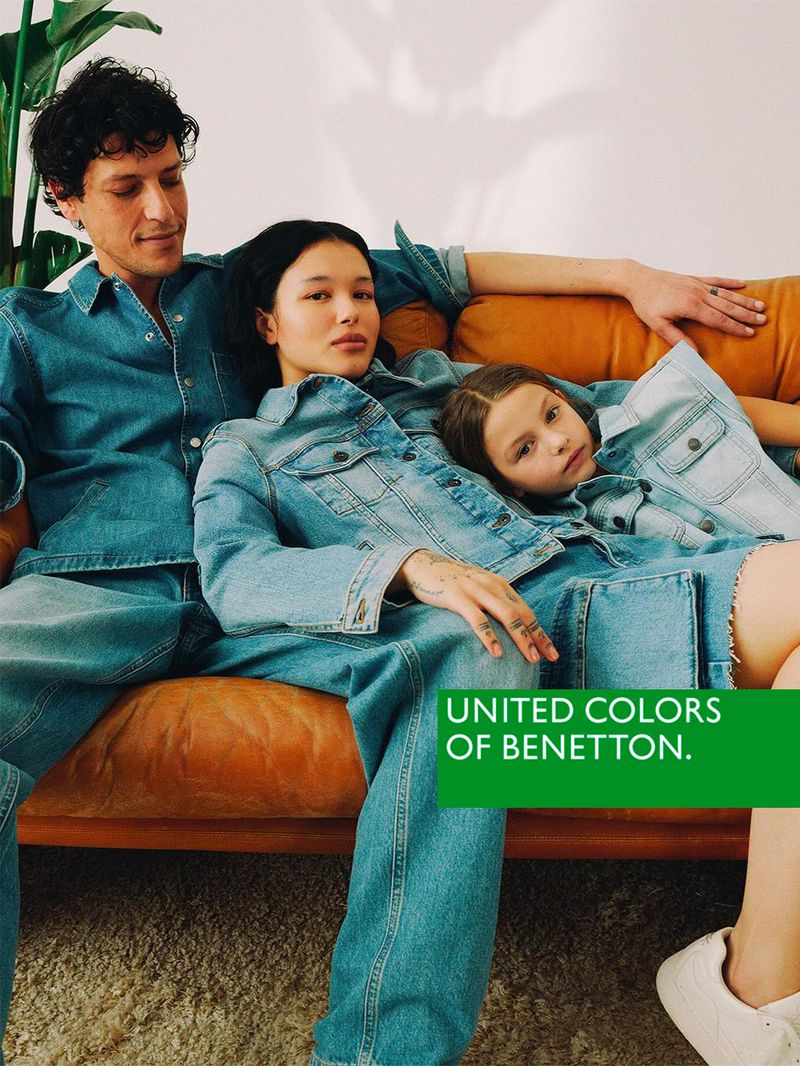 Family fashion campaign on an orange couch featuring a man, woman, and child wearing matching denim apparel with the UNITED COLORS OF BENETTON logo.