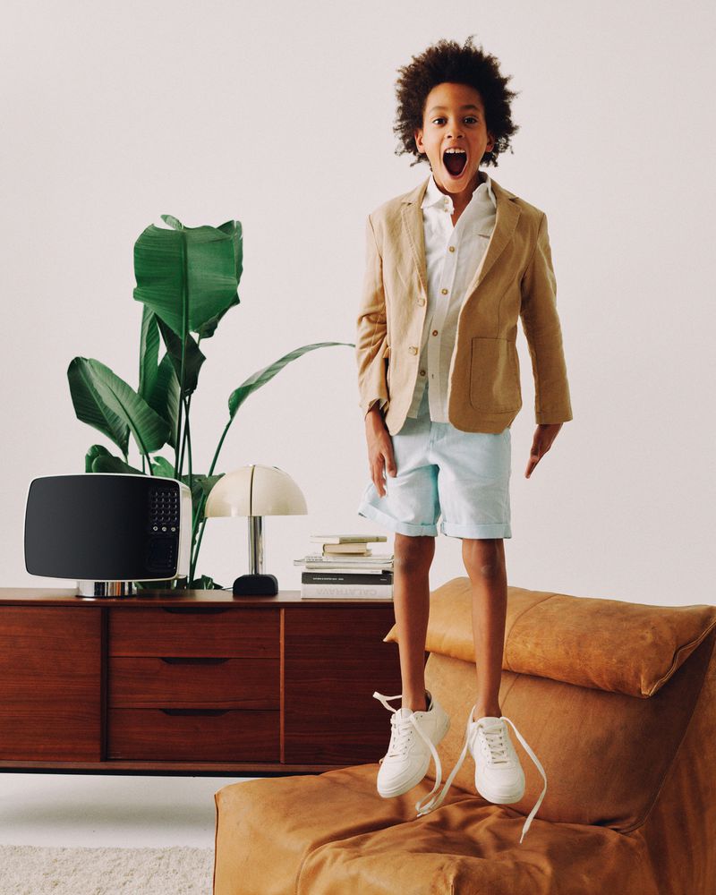 Enthusiastic young boy in a blazer jumps mid-air with open mouth in an indoor setting, adding a playful touch to fashion photography.