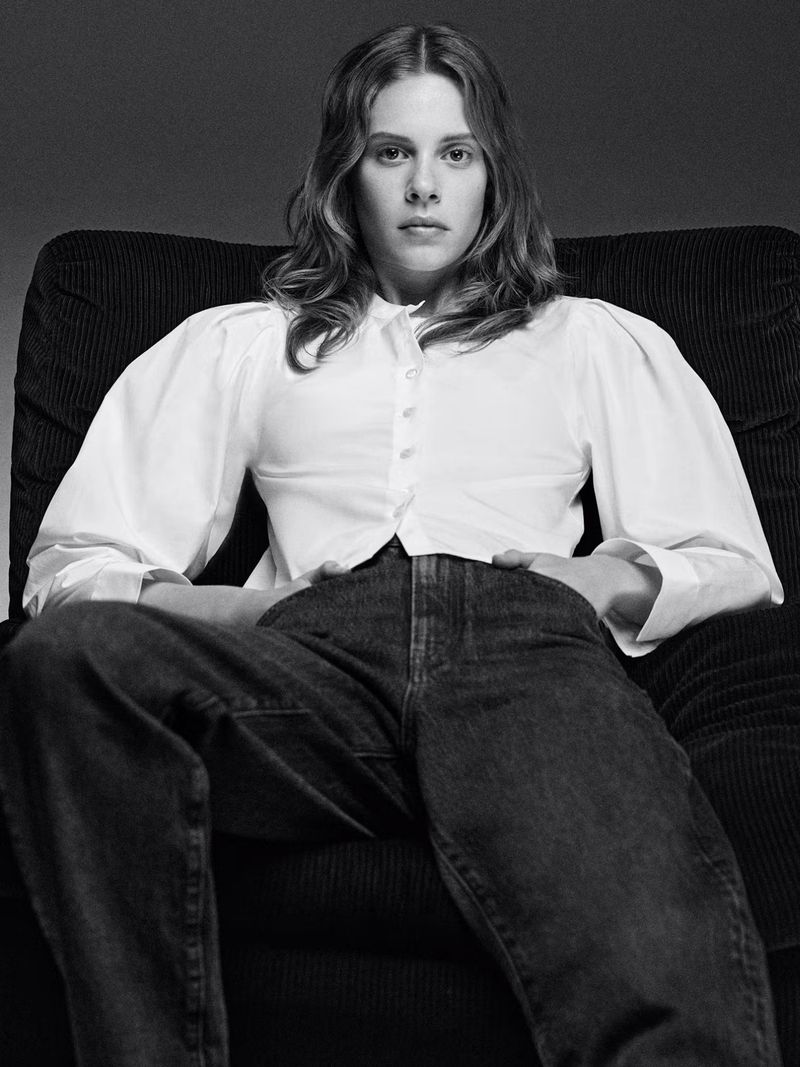 Model Anouk Smits wearing a white button-down shirt and dark denim jeans seated in an armchair for FRAME.