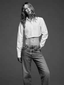 Model wearing a white cropped collared shirt and denim jeans against a grey studio backdrop