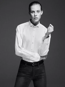 Model in white buttoned shirt and dark trousers standing against a seamless dark studio background