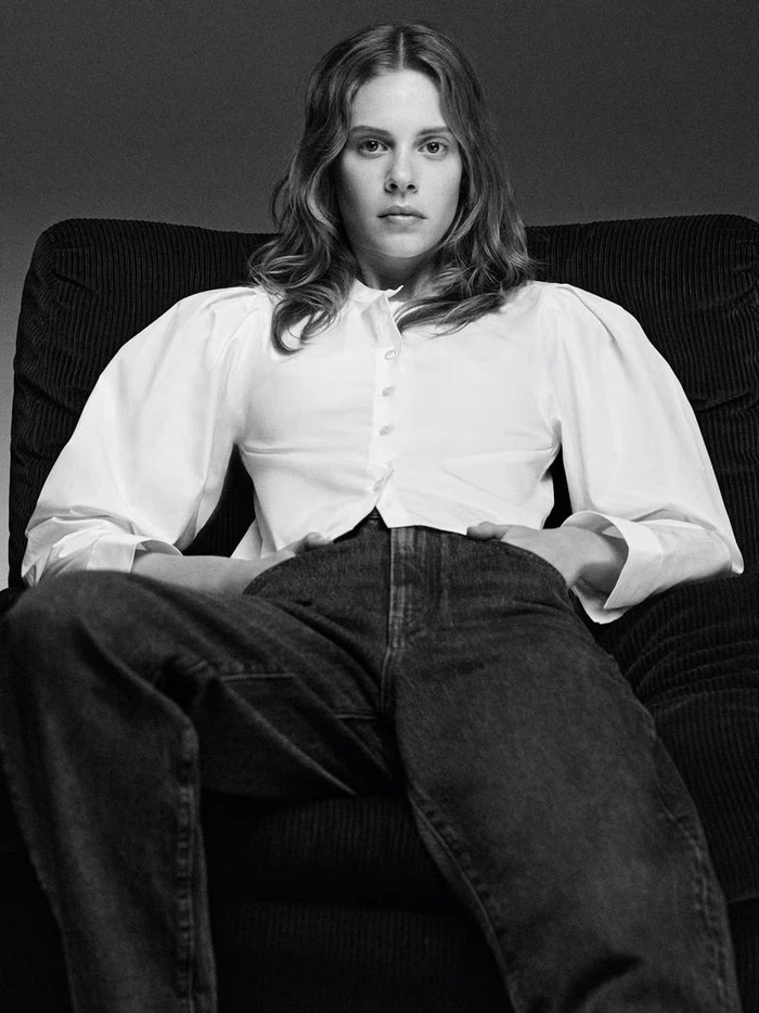 Model Anouk Smits wearing a white button-down shirt and dark denim jeans seated in an armchair for FRAME.