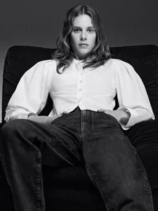 Model Anouk Smits wearing a white button-down shirt and dark denim jeans seated in an armchair for FRAME.