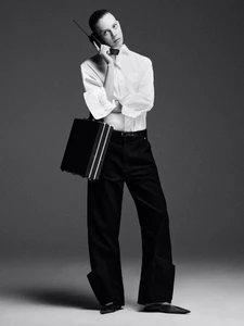Model in white button-down shirt and black trousers holding a vintage phone and briefcase against grey backdrop
