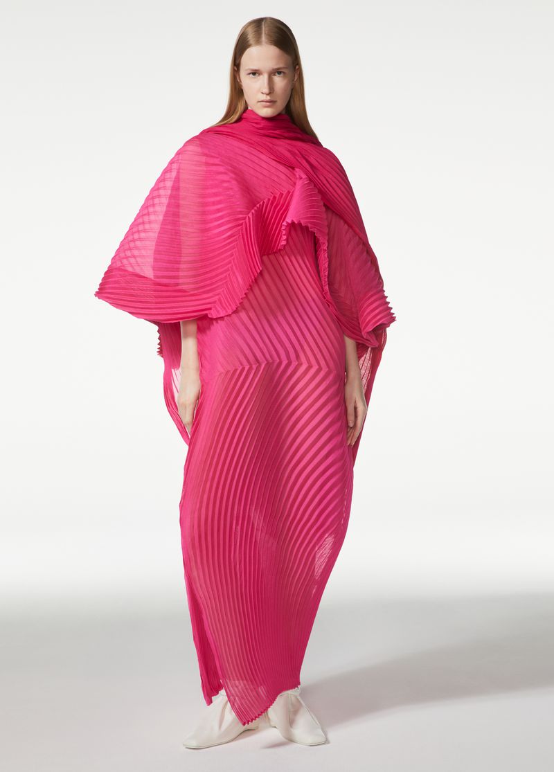Fashion model in a pink pleated dress poses in a bright studio, showcasing an elegant and textured garment with a unique design.