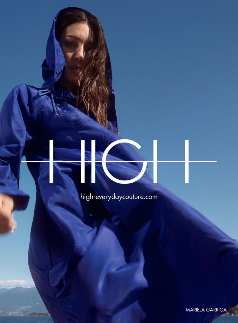 Woman in hooded blue jacket stands against a blue sky and water backdrop with the text "HIGH" overlaid on the image.