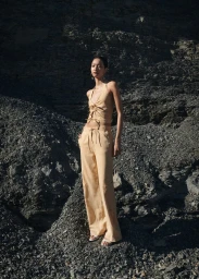 Model standing outdoors on dark rocky terrain wearing a beige halter top and matching trousers for Mango Stripes Arizona