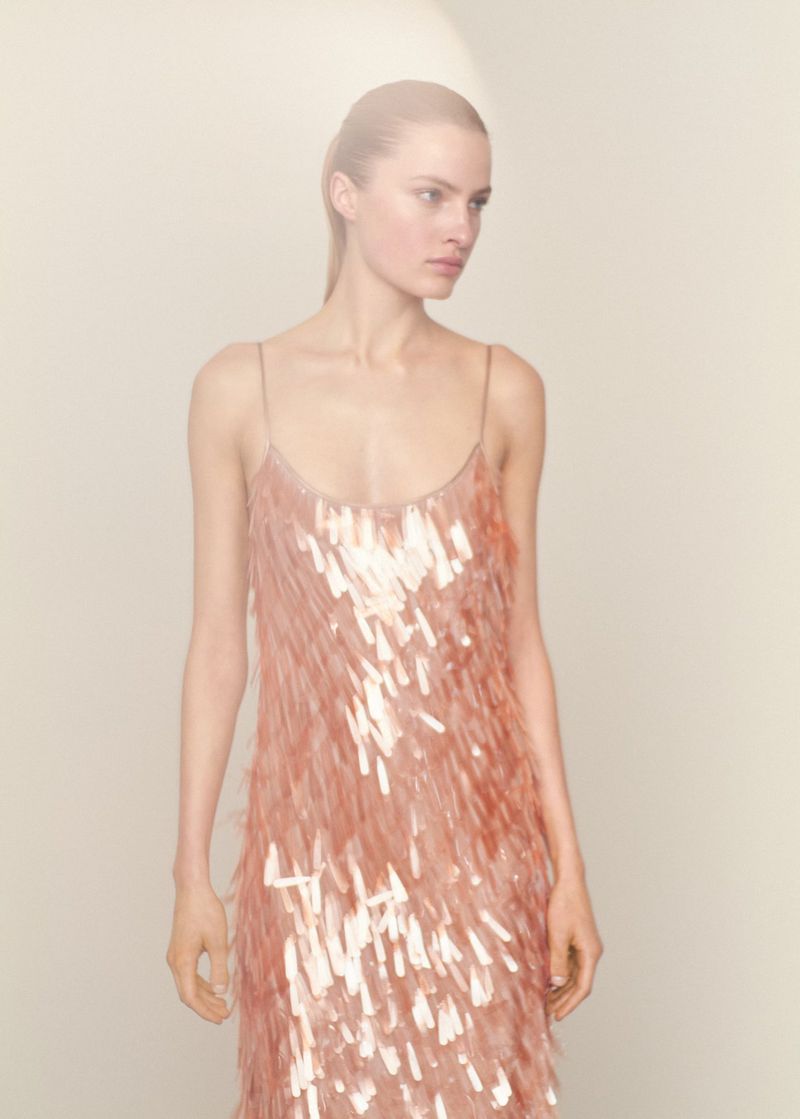 Model Felice Nova Noordhoff wearing a shimmering rose pink sequin fringe slip dress against an off-white studio background.