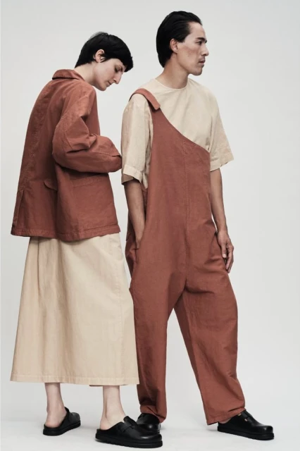 Two models present rust-colored jumpsuits and jackets with neutral skirts against a clean white backdrop, showcasing contemporary fashion.