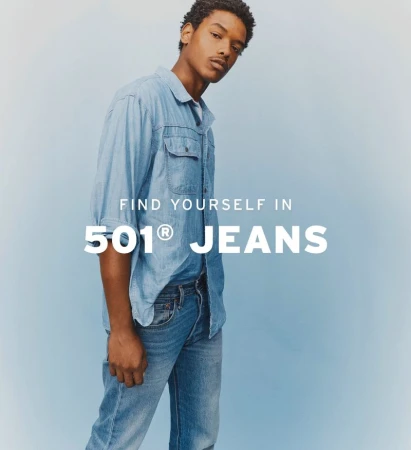 A young adult male poses in a light blue denim shirt and jeans in front of a light blue background for a fashion advertisement.