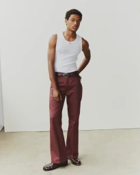 Nile Winchester standing in a white ribbed tank top and burgundy flared trousers against a clean studio backdrop.