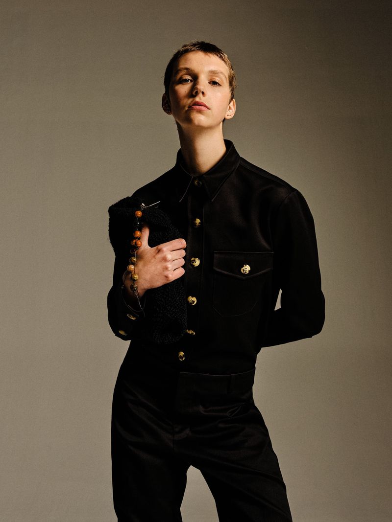 A person in a dark suit poses with a fuzzy black bag, accentuated by a shallow depth of field in a fashion editorial style.
