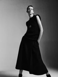 Model with short hair wearing a dark sleeveless top and long skirt against a grey backdrop