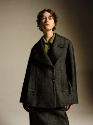 Model Bente Oort wears a dark charcoal wool jacket over an olive green collared shirt against a neutral studio backdrop.