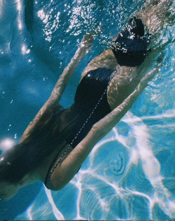Underwater view of a woman swimming in a pool, with sunlight creating patterns on the pool's floor and sides.