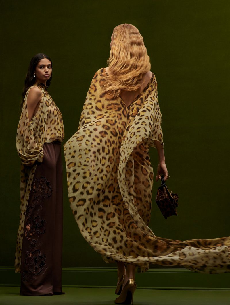 Two women in a studio setting wearing dresses with a leopard print pattern, one facing the camera, the other with her back to the camera.