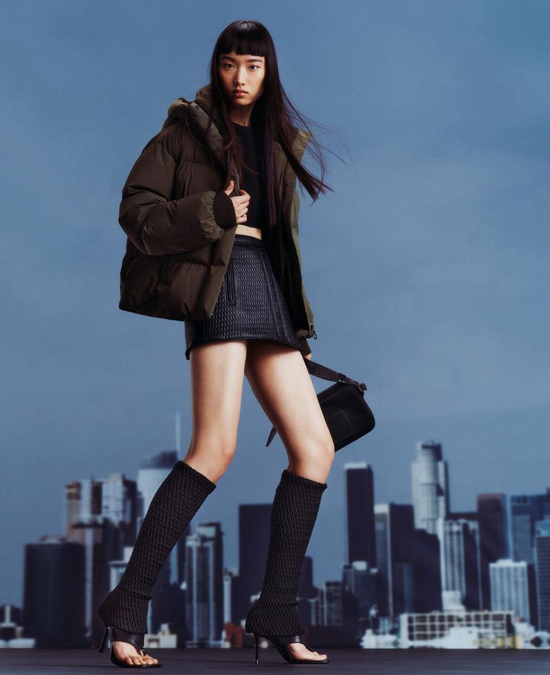 An Asian woman models outerwear and legwear in a full shot against a skyline backdrop, showcasing fashion apparel and accessories.