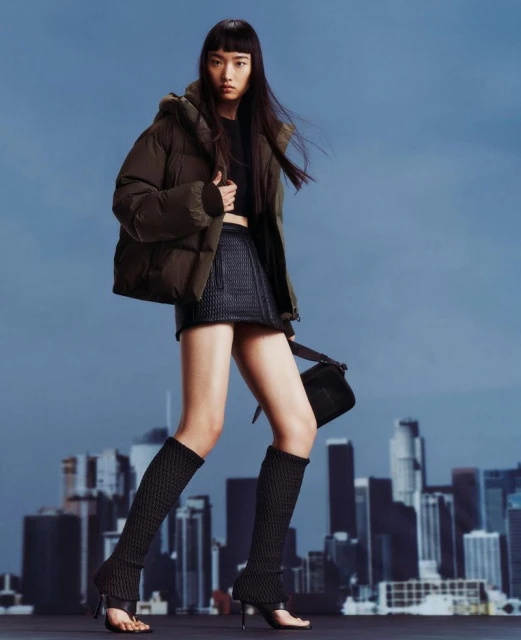 An Asian woman models outerwear and legwear in a full shot against a skyline backdrop, showcasing fashion apparel and accessories.