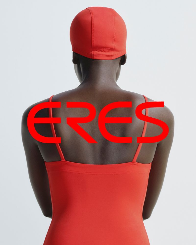 Rear shot of a dark-skinned adult female in red swimwear and matching swim cap against a white backdrop with overlaid red text.