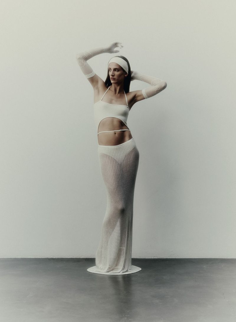 Elegant woman in a cut-out knit halter dress with sheer knit gloves and a matching headband, posing against a neutral backdrop in a studio setting.