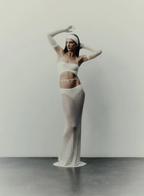 Elegant woman in a cut-out knit halter dress with sheer knit gloves and a matching headband, posing against a neutral backdrop in a studio setting.