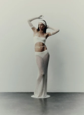 Elegant woman in a cut-out knit halter dress with sheer knit gloves and a matching headband, posing against a neutral backdrop in a studio setting.