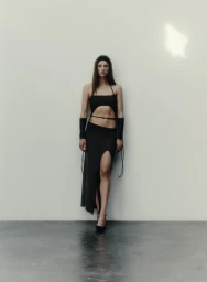 Model wearing a long textured burgundy coat, matching bralette, and mini skirt against a neutral studio wall.