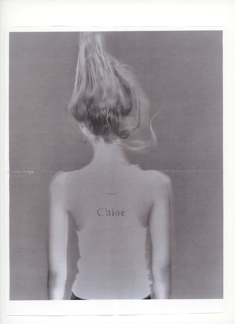 Rear view of model Ida Heiner with hair styled upwards wearing a light tank top with Chloé printed on the back in a studio setting.