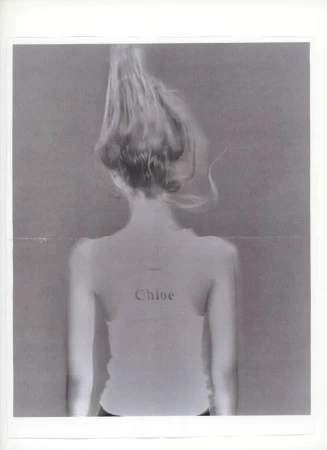 Rear view of model Ida Heiner with hair styled upwards wearing a light tank top with Chloé printed on the back in a studio setting.