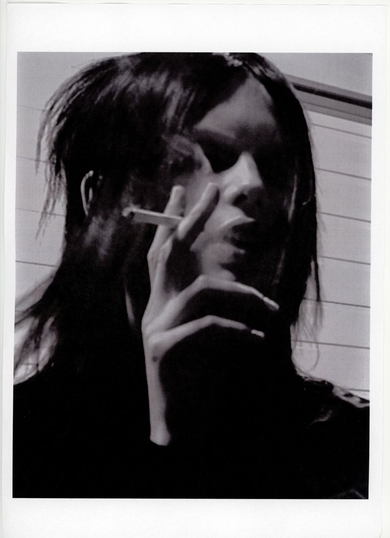 Monochromatic portrait of a woman smoking a cigarette, showcasing chiaroscuro lighting and a contemplative mood in a minimalist setting.