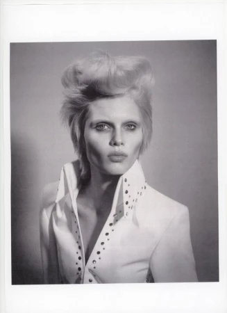 Monochrome portrait of adult woman with blonde hair styled in a high pompadour, wearing white collared shirt with studded trim. 