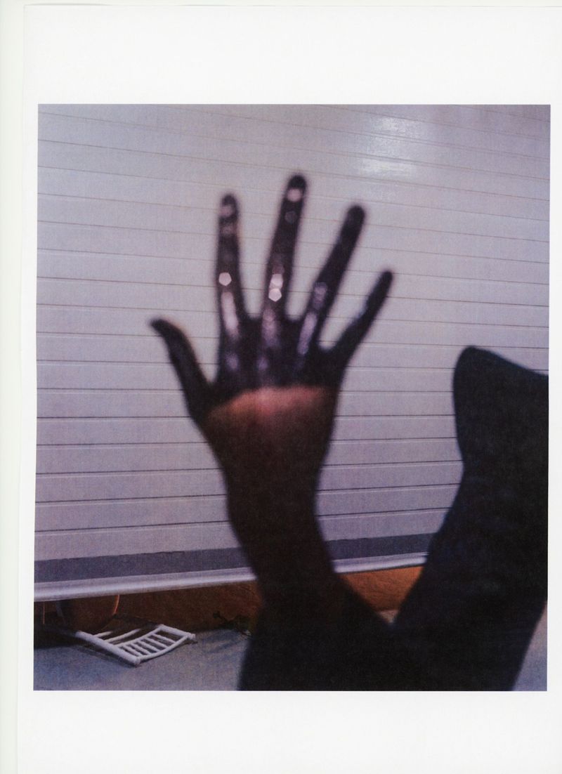 Abstract photograph featuring an outstretched human hand covered in a dark substance against a light background, creating contrast.