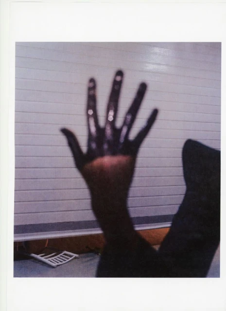 Abstract photograph featuring an outstretched human hand covered in a dark substance against a light background, creating contrast.