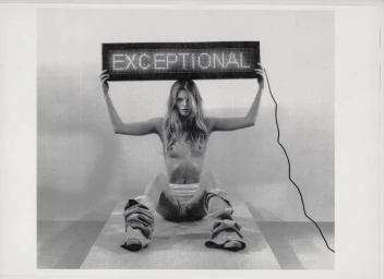 Model Ida Heiner holding an illuminated LED sign reading EXCEPTIONAL in a black and white editorial portrait photograph.
