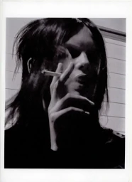 Black and white portrait of model Ida Heiner holding a cigarette to her mouth with dramatic shadows across her face.