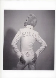 Model Ida Heiner photographed from behind in a white studded jumpsuit with EQUAL embellished on the back against a studio backdrop.