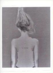 Rear view of model Ida Heiner with hair styled upwards wearing a light tank top with Chloé printed on the back in a studio setting.