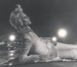 Model with styled light hair wearing an embellished white jumpsuit lying outdoors at night