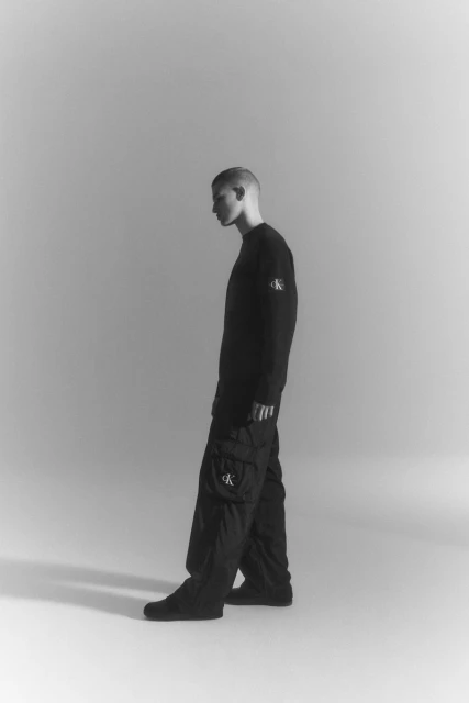 A single male model in black Calvin Klein sweatpants and sweatshirt posing in a photo studio, captured in a high-contrast black and white shot.
