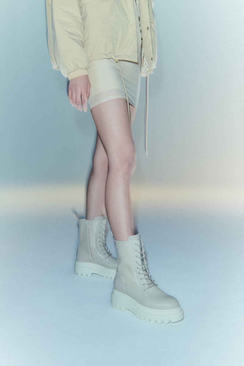 Standing woman in beige jacket and mini-skirt with platform combat boots, studio lighting, fashion editorial.