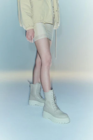 Standing woman in beige jacket and mini-skirt with platform combat boots, studio lighting, fashion editorial.