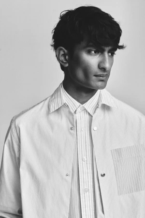Model Rishi Robin in a striped collared shirt and jacket in a black and white studio portrait for BOSS Spring Summer 2024.