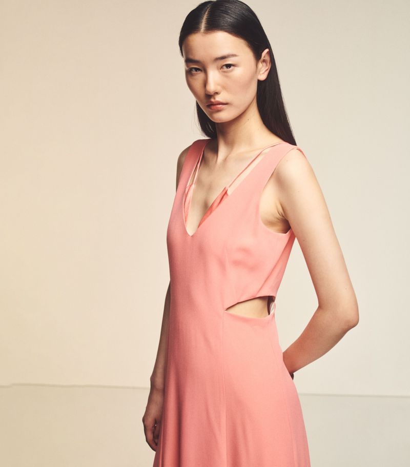 Portrait of a young adult Asian woman in a stylish peach dress with a V-neckline and a side cutout, posing in a studio with neutral background.