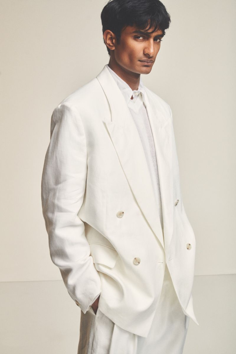 Portrait of a young adult man in a double-breasted white suit, set against a neutral backdrop, showcasing a modern, elegant fashion style.