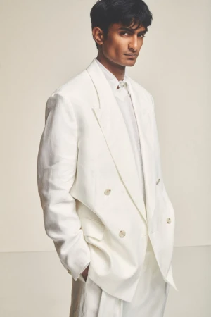 Portrait of a young adult man in a double-breasted white suit, set against a neutral backdrop, showcasing a modern, elegant fashion style.
