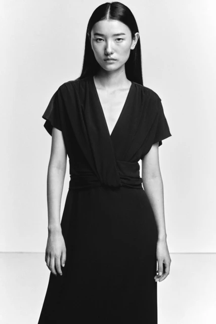 Portrait of a woman with long dark hair wearing a dark dress against a white background in a studio. Fashion shot in black and white.