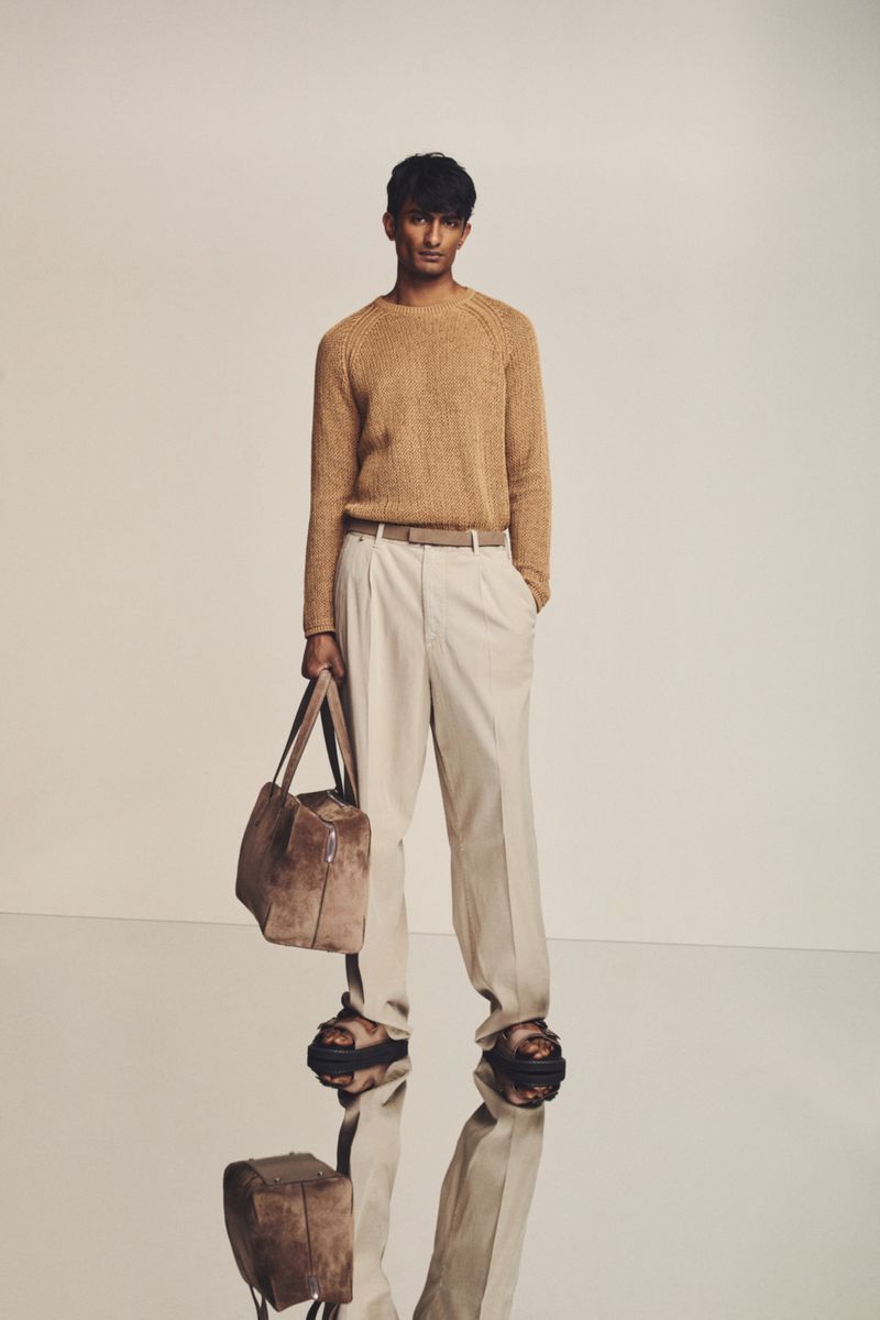 A full-length studio shot showcases a dark-haired man wearing a tan sweater, cream slacks, and sandals, carrying a tote bag.