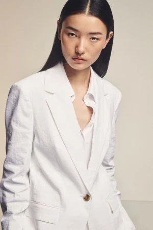 Model Houjing Cui wearing an oversized white tailored blazer and white shirt against a neutral studio backdrop.