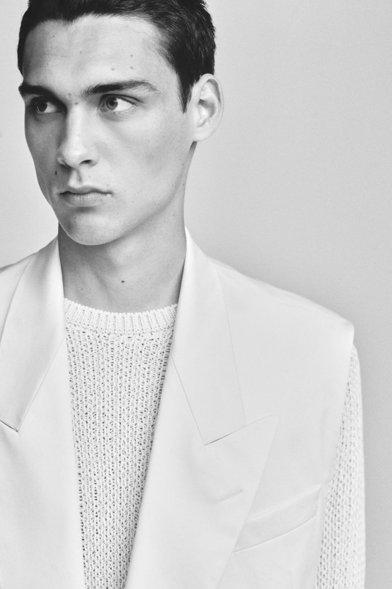 Black and white portrait of a young adult male in a white knit sweater and matching suit jacket, gazing slightly to the left.